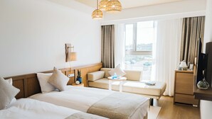 Quarto de hotel com duas camas, um sofá, uma mesinha, uma televisão e uma janela com cortinas.