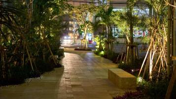 A nighttime pathway lined with bamboo and tropical plants, leading to a building with illuminated windows.