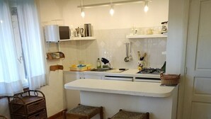 Une cuisine compacte avec un plan de travail blanc, deux tabourets, un petit évier et un four à micro-ondes.