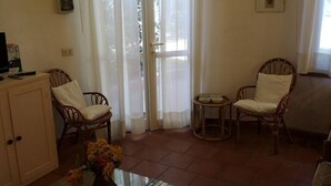 Un salon avec deux fauteuils en osier, une table basse en verre, un meuble et une porte avec des rideaux.