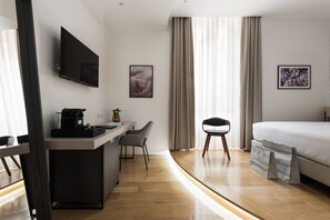 Une chambre d’hôtel moderne équipée d’une télévision à écran plat, d’un bureau avec une machine à café, d’un lit et de deux chaises.