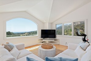 A modern living room with a large TV, comfortable seating, and a scenic view through large windows. - Santa Barbara Hideaway with Terraced Suites (Santa Barbara)