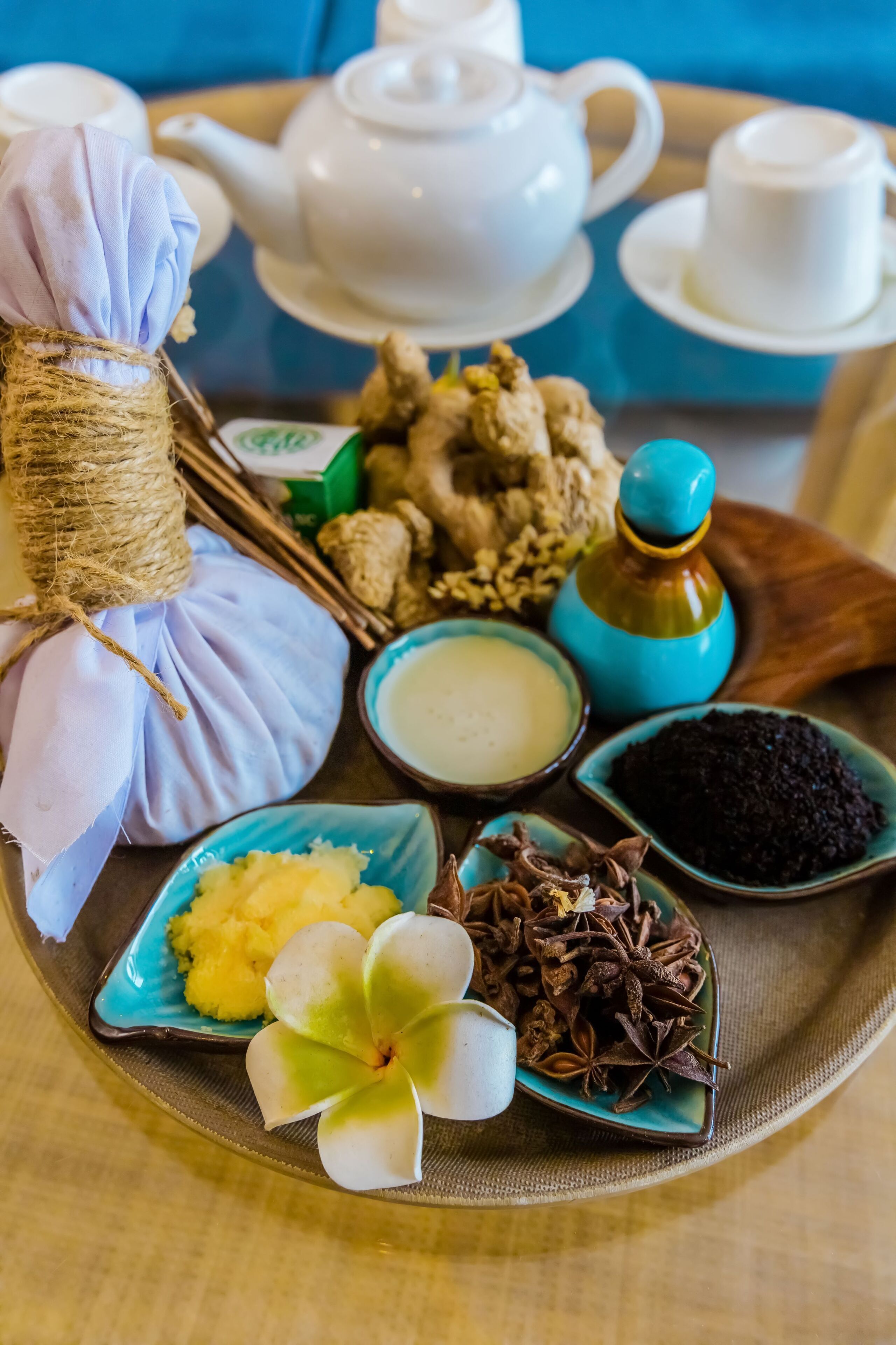 A tray with a white teapot, cups, a blue teapot, ginger, spices, and a flower.