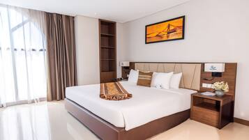 A modern hotel room with a large bed, a wooden headboard, a nightstand with a lamp, and a painting on the wall.