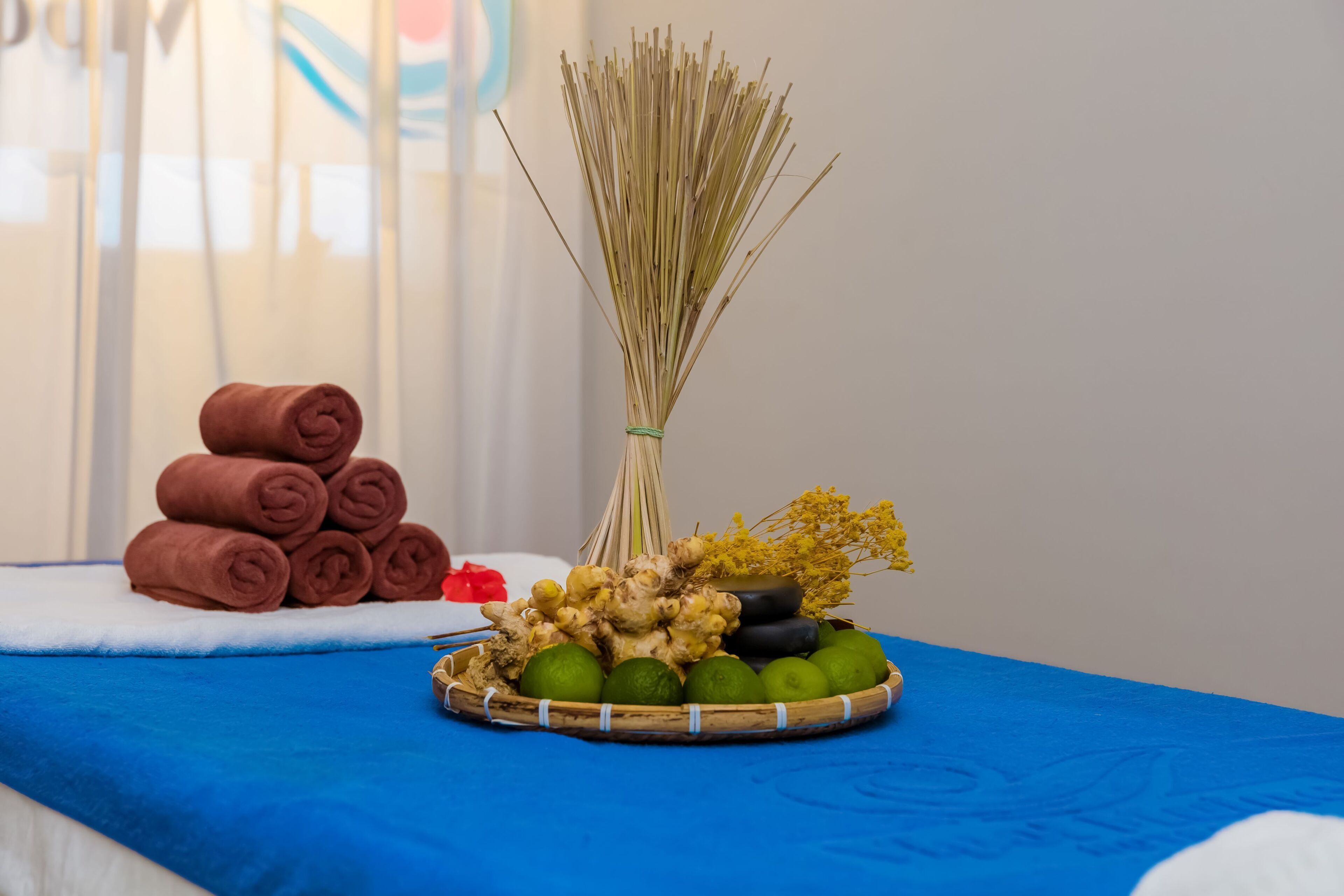 Una mesa de masaje con una toalla azul, una cesta de jengibre y lima, y toallas enrolladas.