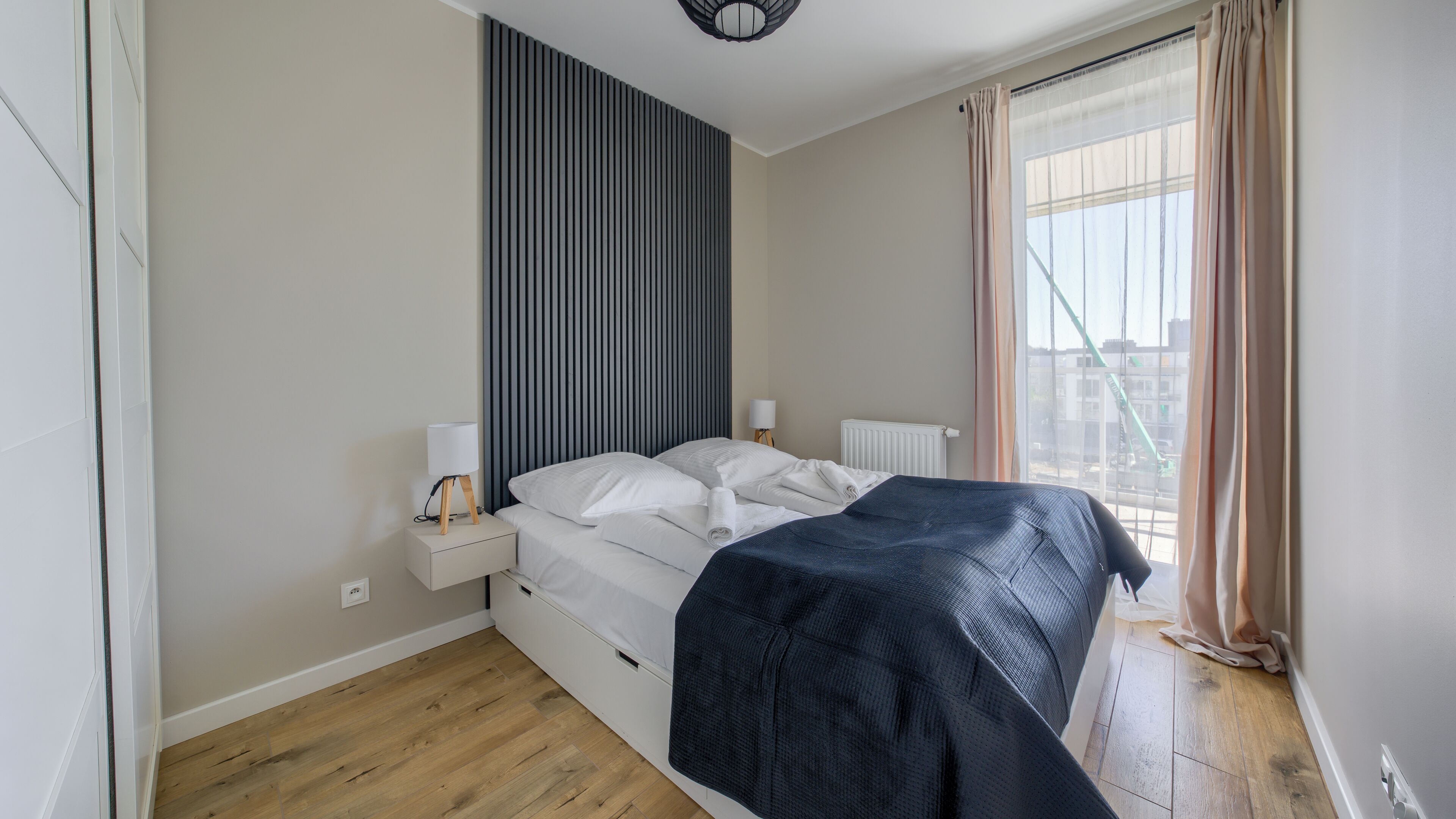 A bedroom with a bed, bedside tables, a lamp, a radiator, and a window with curtains.