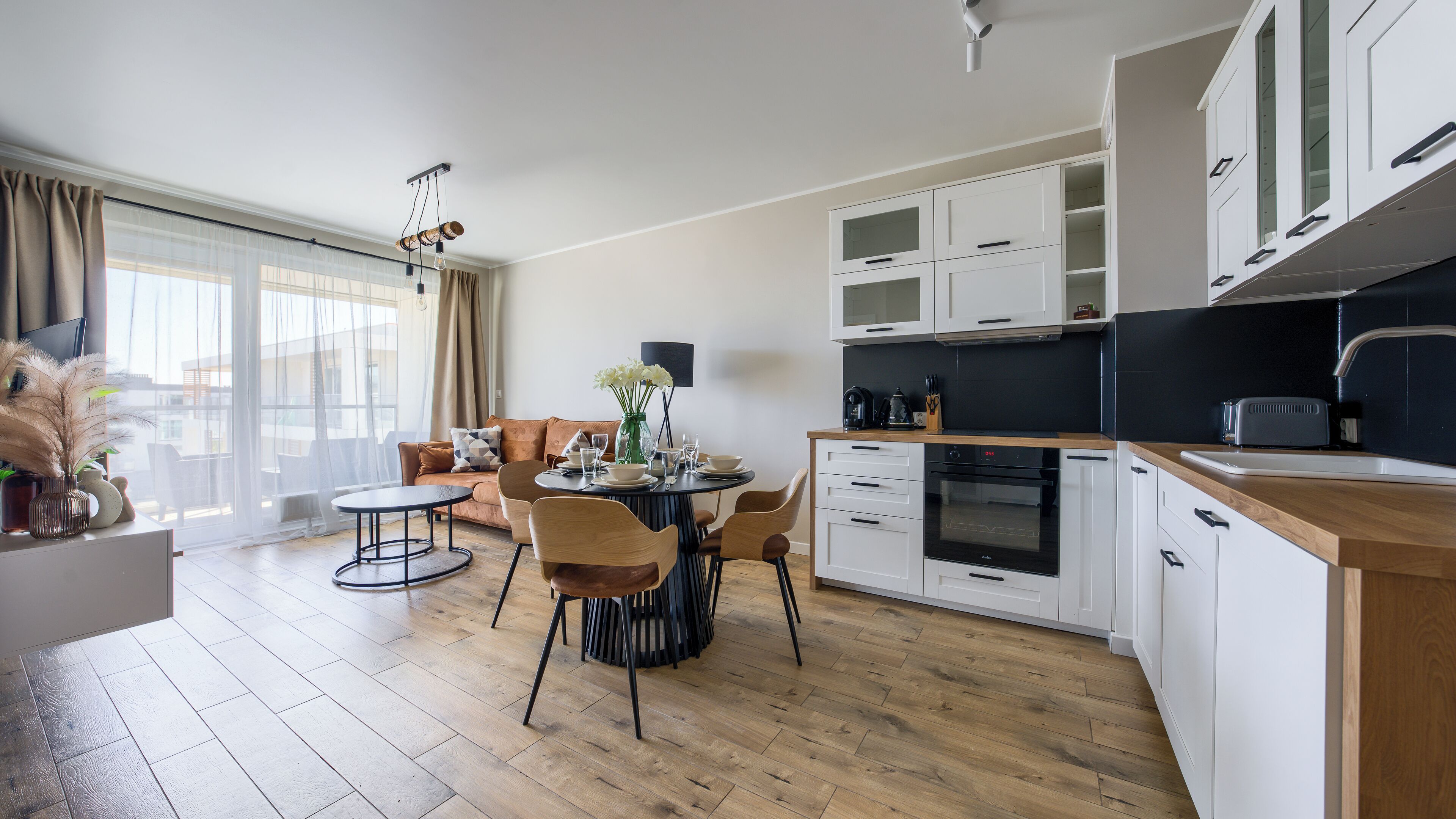 A modern kitchen with white cabinets, a dining area with a round table, and a sofa.