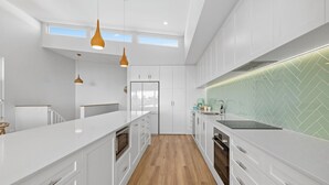 A modern kitchen with white cabinetry, a herringbone tile backsplash, and pendant lighting. - Tea Trees Ocean Views, Pet-Friendly, Walk to shops and Beach (Woolgoolga)