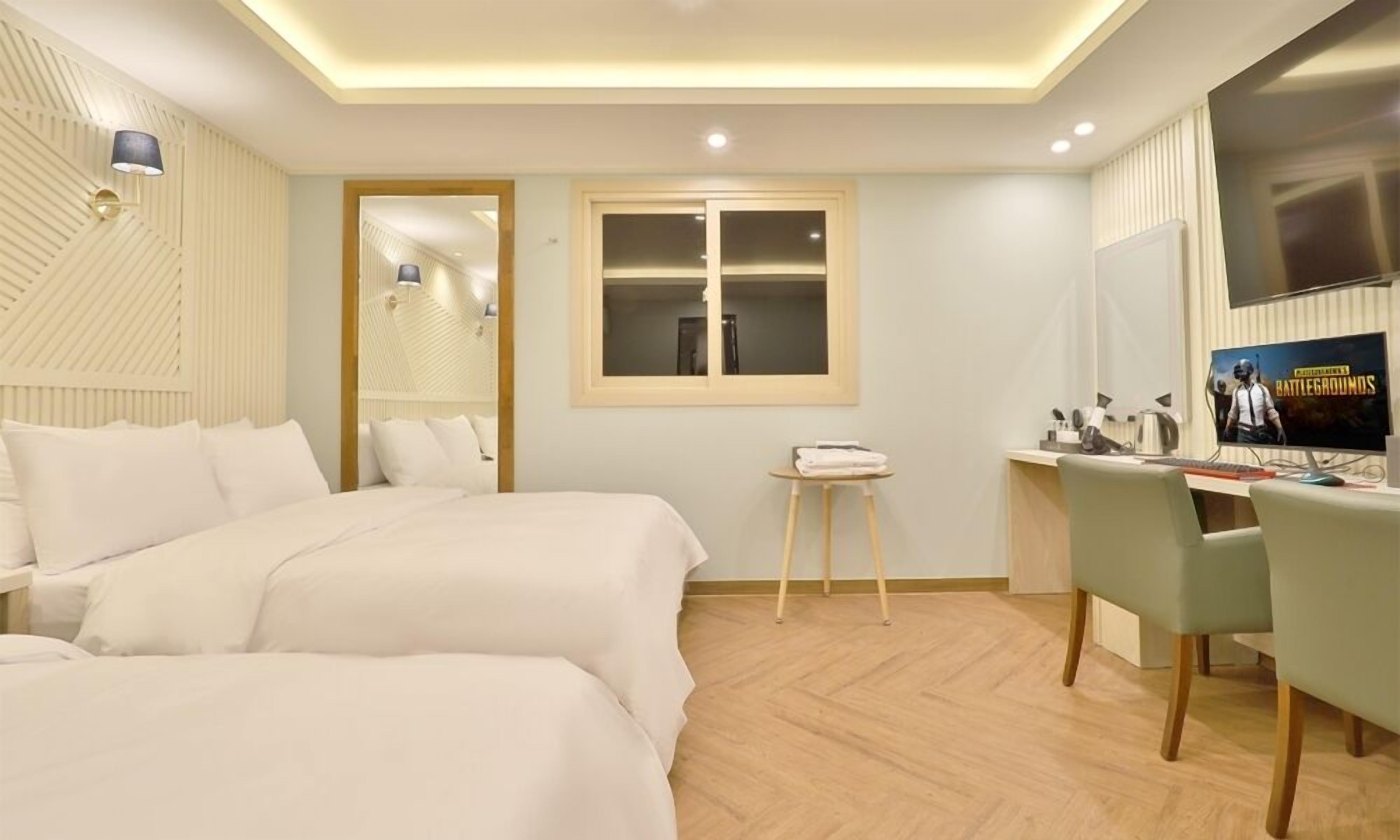 Una habitación de hotel con dos camas, un escritorio con computadora, televisor y ventana.