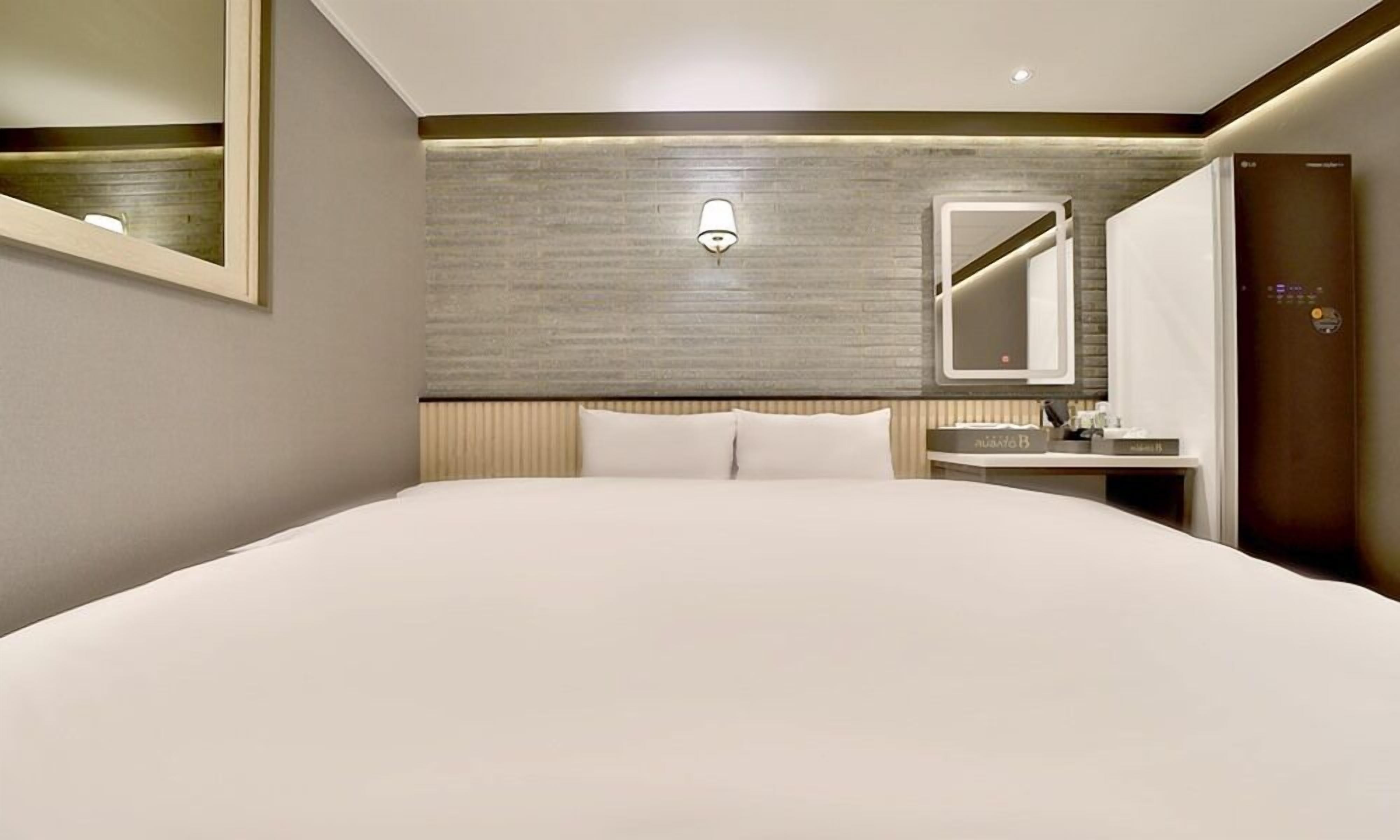 A hotel room with a large bed, a bedside table, a mirror, and a built-in wardrobe.