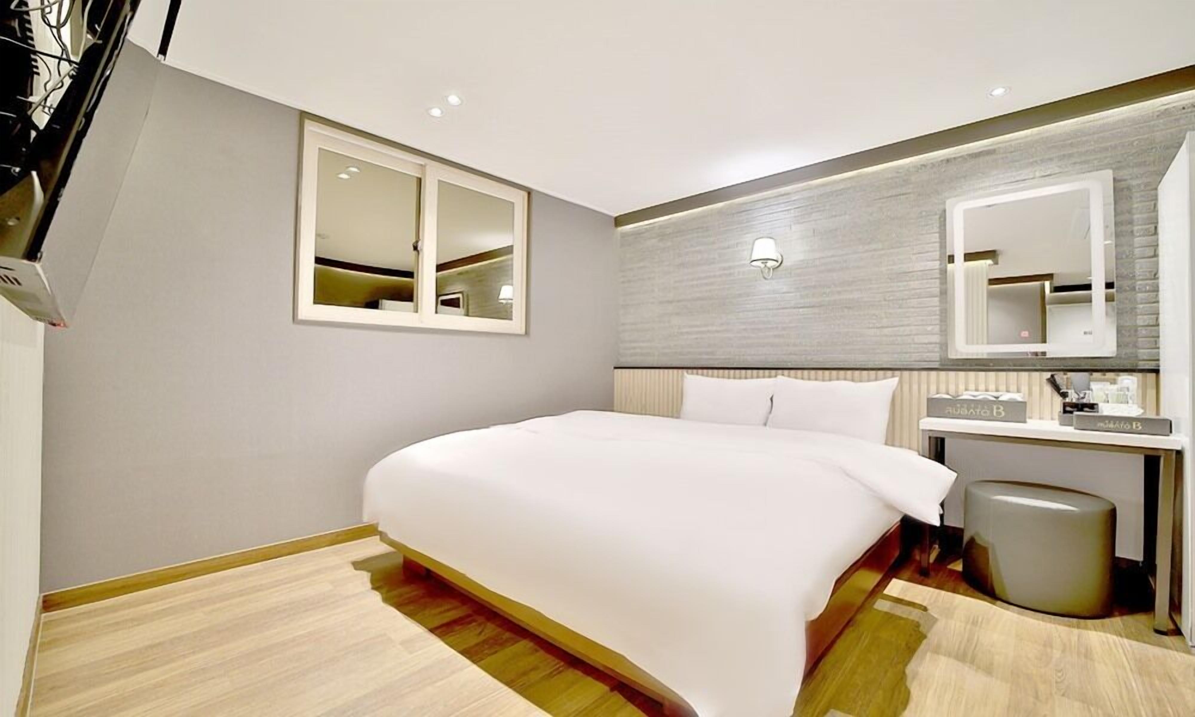 Habitació d'hotel moderna amb un llit gran, una tauleta de nit amb una làmpada, un mirall i un petit safataire.