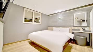 A modern hotel room with a large bed, a bedside table with a lamp, a mirror, and a small trash bin.