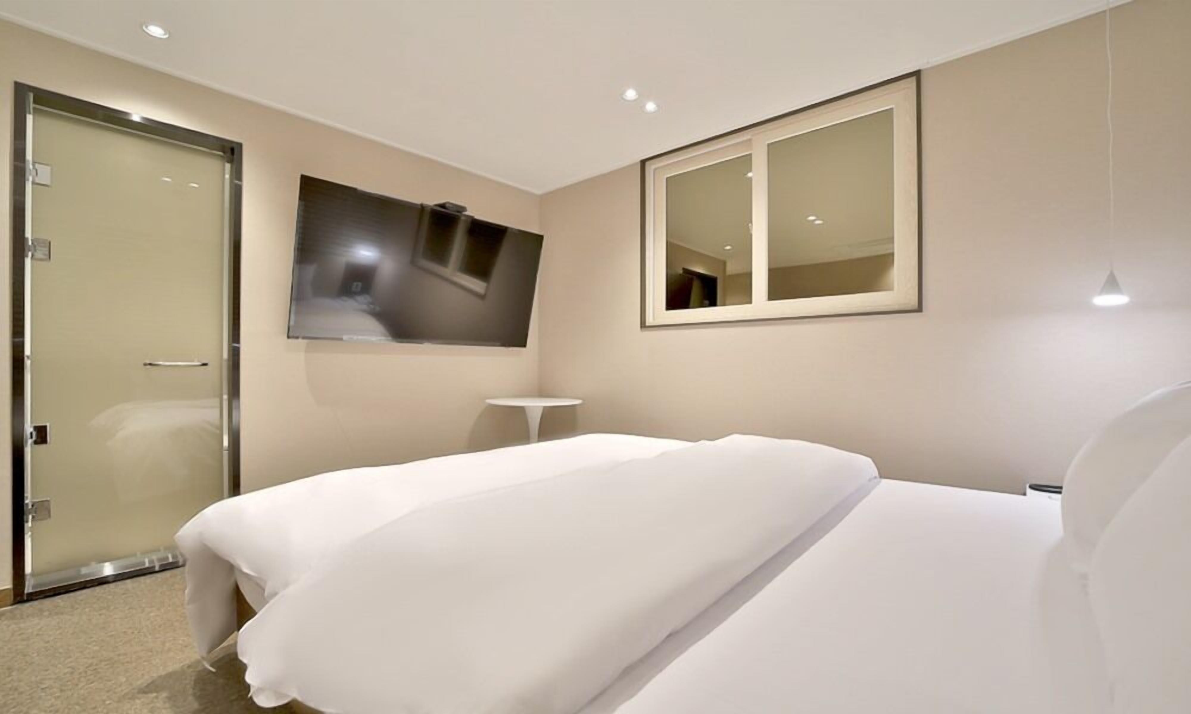 A hotel room with a bed, a small table, a mirror, and a door.