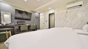 A modern hotel room with a large bed, a desk with a chair, a flat-screen TV, a mirror, and an air conditioning unit.