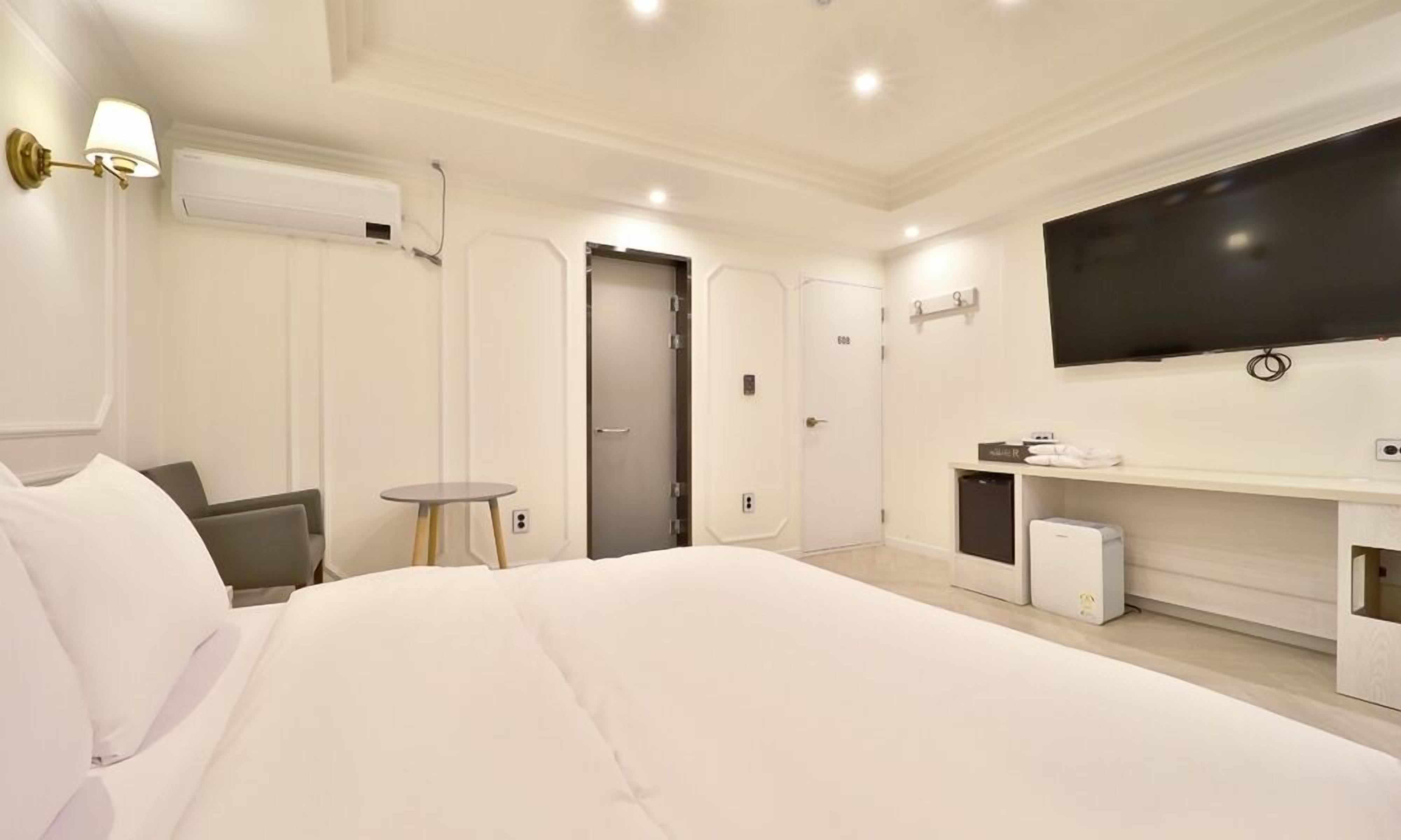 Ein Hotelzimmer mit einem großen Bett, einem kleinen Tisch, einem Fernseher und einer Minibar.