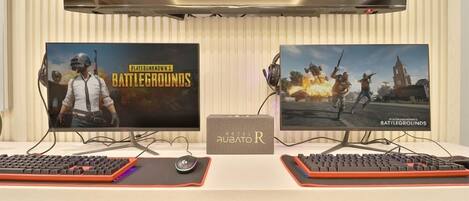 Two monitors displaying 'Battlegrounds' game covers, a keyboard, a mouse, and a 'Hotel Rubato R' sign.