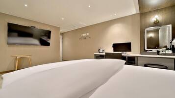 Una habitación de hotel moderna con una cama grande, un escritorio con computadora, un televisor de pantalla plana y un espejo amplio.