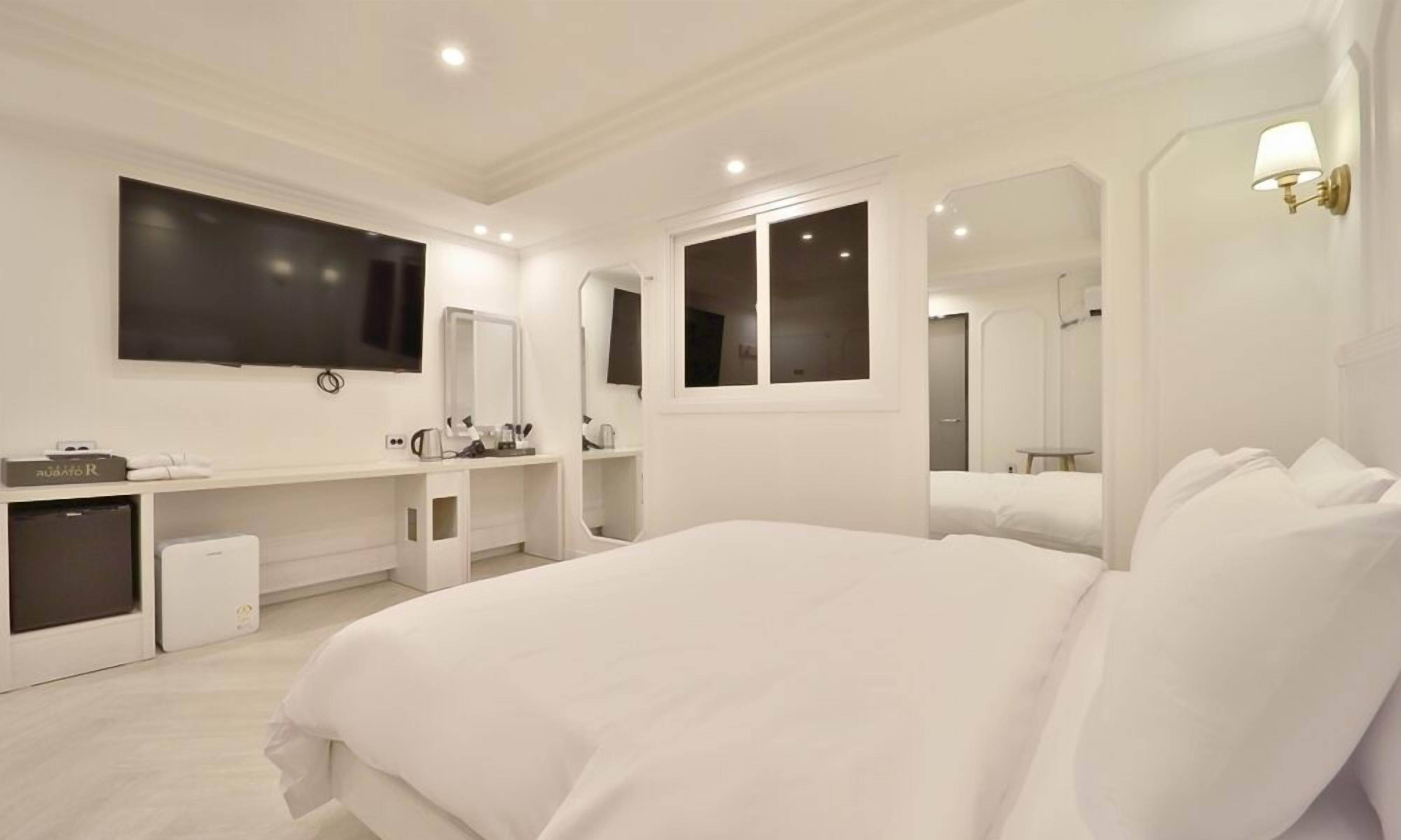 Una habitación de hotel moderna con una cama grande, un televisor montado en la pared, un escritorio con espejo y una ventana.