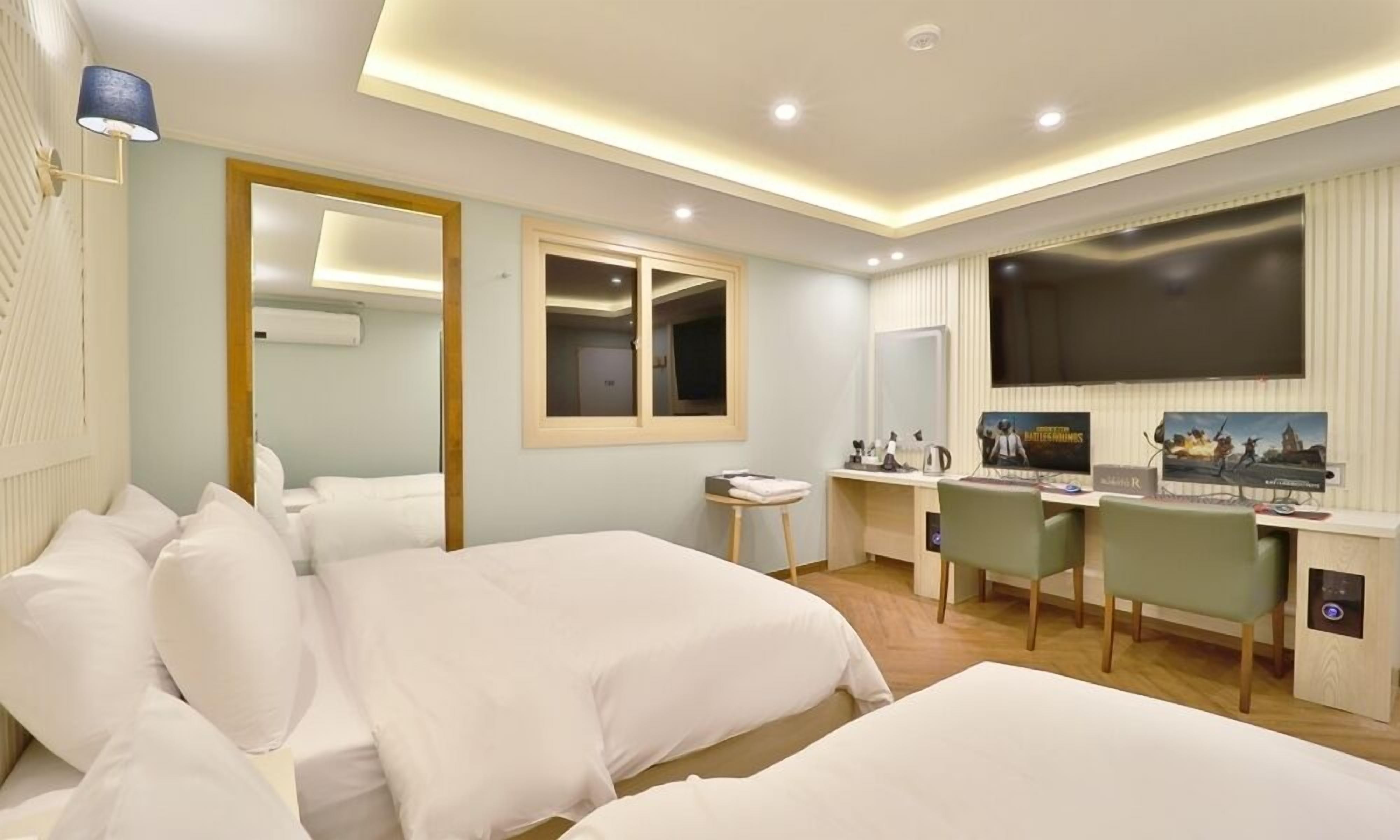 A hotel room with two beds, a desk with a chair, a large TV, and a mirror.
