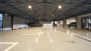 A spacious indoor parking area with a high ceiling and metal beams. There are two cars parked, and the floor has directional arrows. - HOTEL RUBATO RB (Daegu)