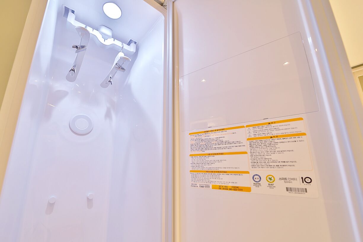 Une salle de bain avec un lavabo blanc, deux robinets et un miroir. Un panneau avec du texte et des symboles est fixé au mur.