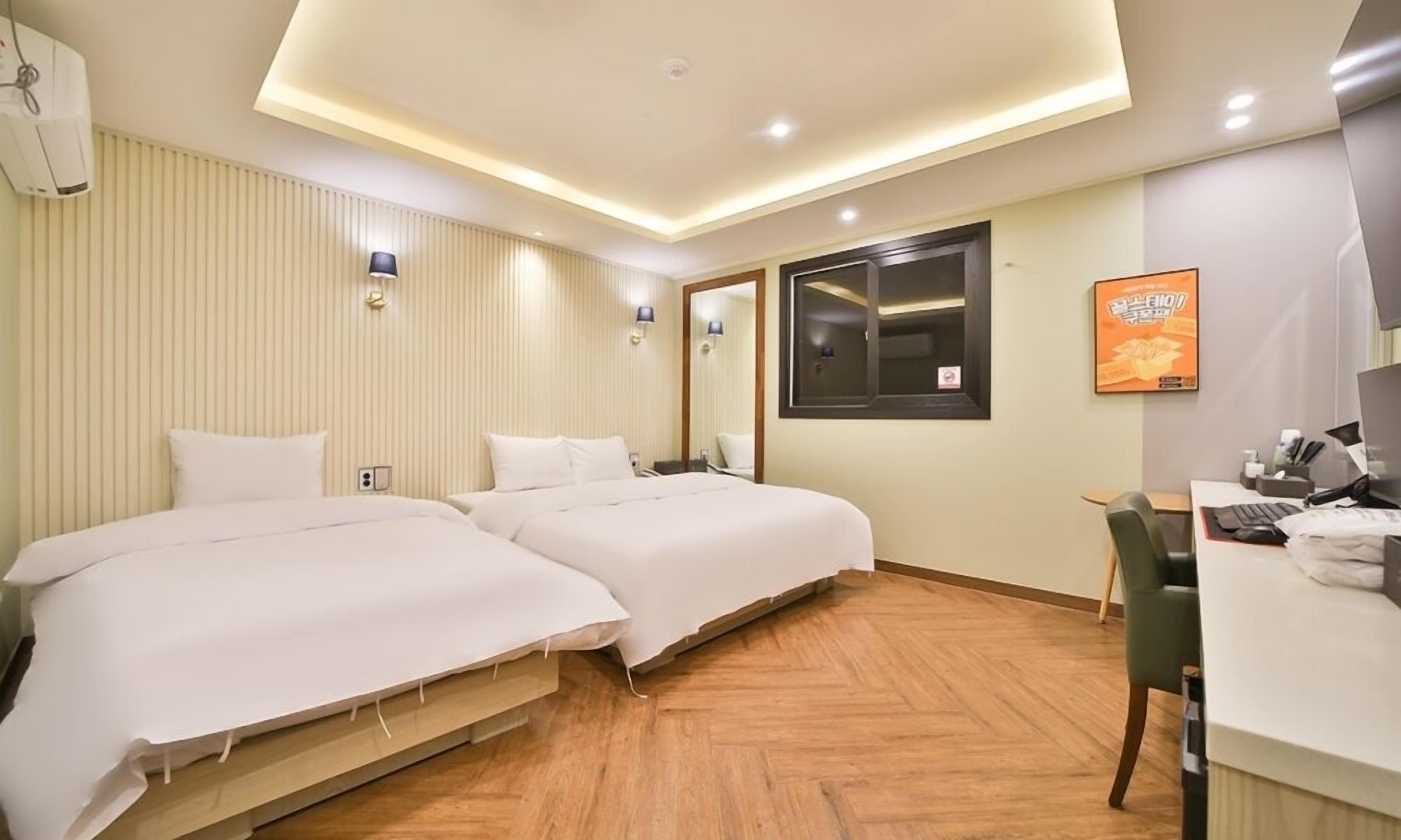 A hotel room with two beds, a desk with a computer, and a window with blinds.