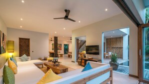 A modern living room with a large sofa, wooden coffee table, and a TV. There is a staircase leading to an outdoor area. - Puri Aman - Unique & Lush 3BR Pool Villa - Next to Gigi Susu & Walk to Beach (Canggu)