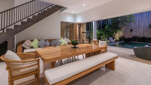 A modern living room with a wooden dining table, wicker chairs, a bench, and a staircase. - Puri Aman - Unique & Lush 3BR Pool Villa - Next to Gigi Susu & Walk to Beach (Canggu)