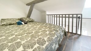 Un dormitorio con techo inclinado, cama con ropa de cama estampada, viga de madera y balcón con barandilla.