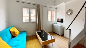 Una sala de estar moderna con un sofá azul, una mesa de centro de vidrio y una mesita auxiliar blanca con un televisor.