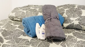 Una cama con ropa de cama estampada, una toalla azul doblada, una toalla gris doblada y una botella de jabón Dove para el cuerpo.