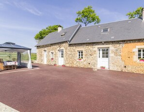 Un bâtiment en pierre avec un toit rouge, un espace extérieur couvert avec des sièges et une allée pavée.