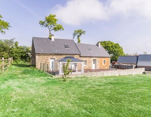 Une maison en pierre avec un toit en pente, un petit jardin et un espace extérieur aménagé avec des sièges.