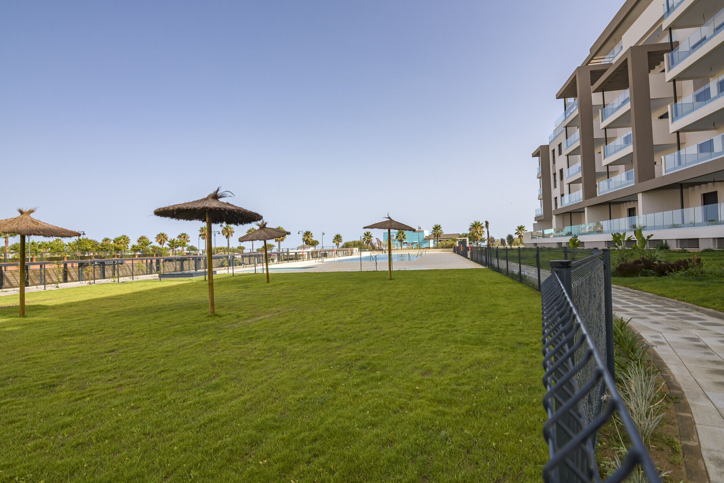 Un'area verde con ombrelloni, una piscina e un edificio moderno con balconi.