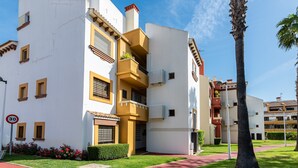 Un edificio residencial de varios pisos con balcones, un sendero de ladrillo rojo y una palmera.