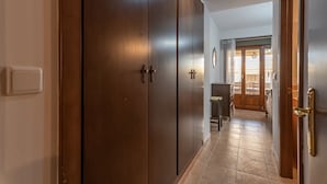 Un pasillo con puertas de madera, un interruptor de luz y un suelo de baldosas que conduce a una habitación con una puerta y una ventana de madera.