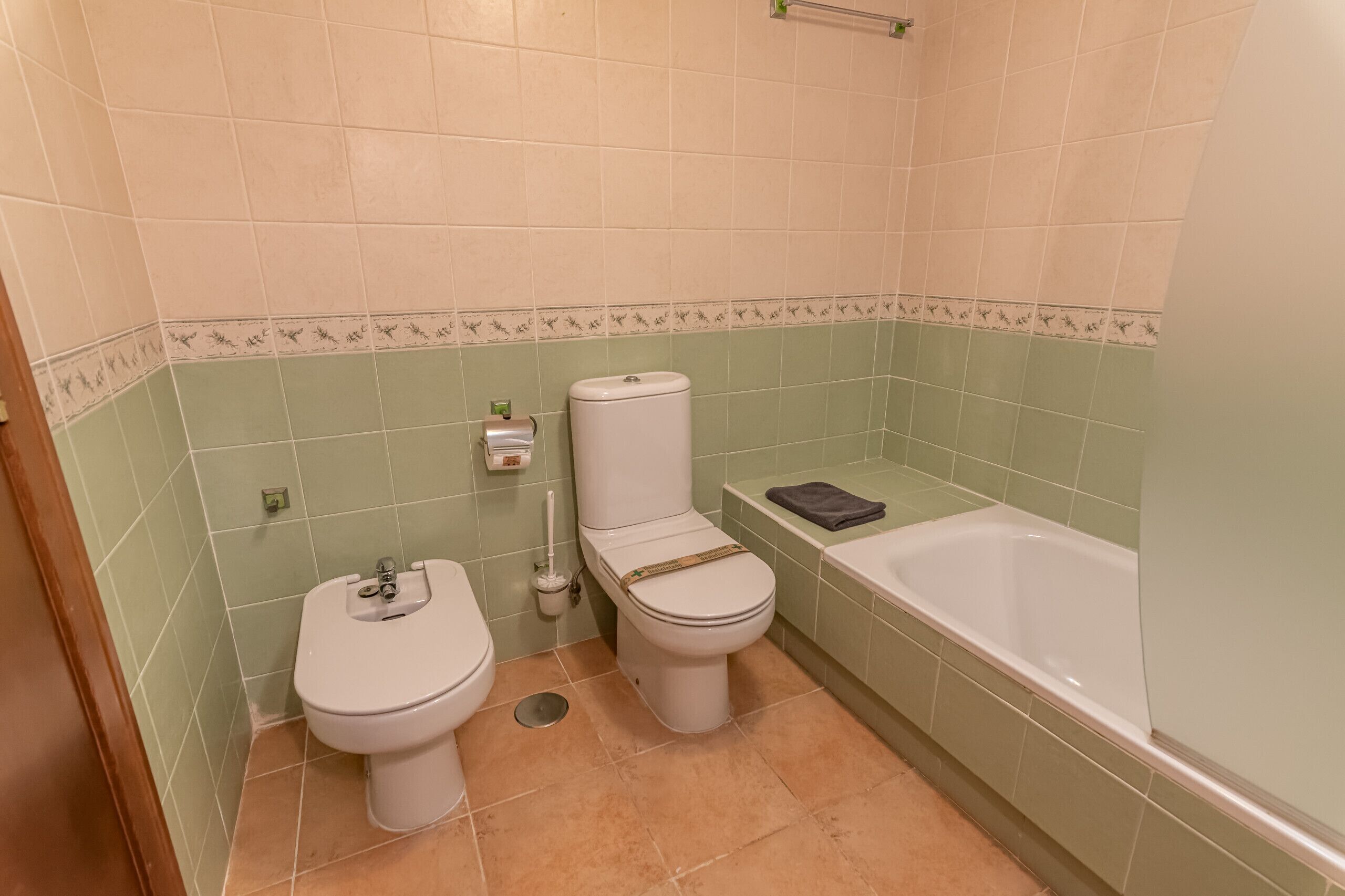 A bathroom with two toilets, a bathtub, and a toilet paper dispenser.