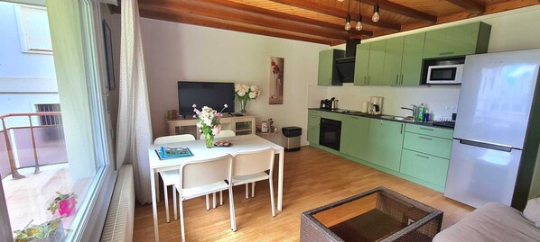 Una cocina moderna con armarios verdes, un refrigerador blanco y una zona de comedor con mesa y sillas.