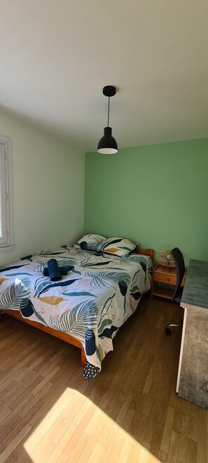 Ein Schlafzimmer mit einem Bett, einem Schreibtisch, einem Stuhl, einer Pendelleuchte und einem Fenster.
