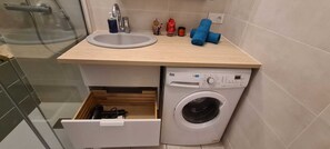 Un baño pequeño con lavamanos, lavadora y un pequeño cajón de almacenamiento.
