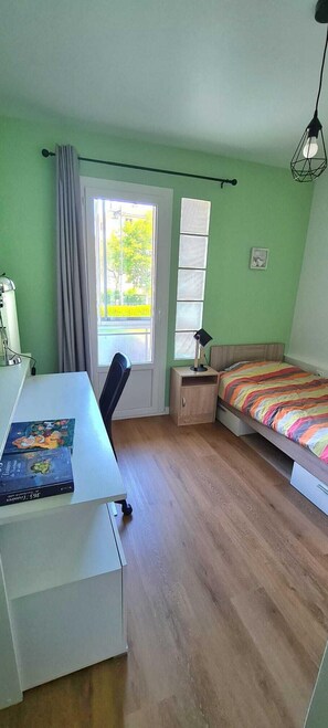 Una habitación con una cama, un escritorio y una silla. Hay una ventana con cortinas, una lámpara y un cuadro en la pared.