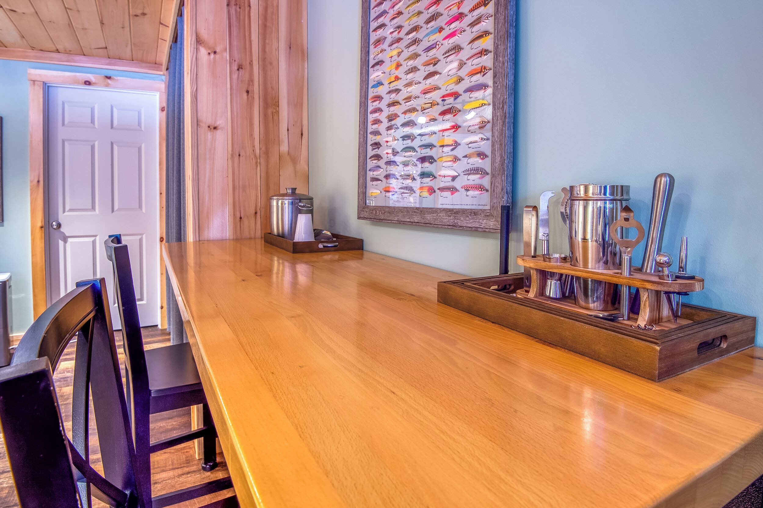 A wooden dining table with chairs, a framed fish collection, and a coffee maker on the table.