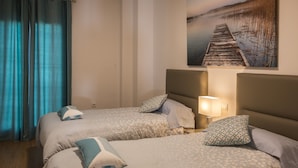 Ein Hotelzimmer mit zwei Betten, jeweils mit gemusterten Bettwaren und Kissen, einem Nachttisch mit Lampe sowie einem Bild eines Piers an der Wand.