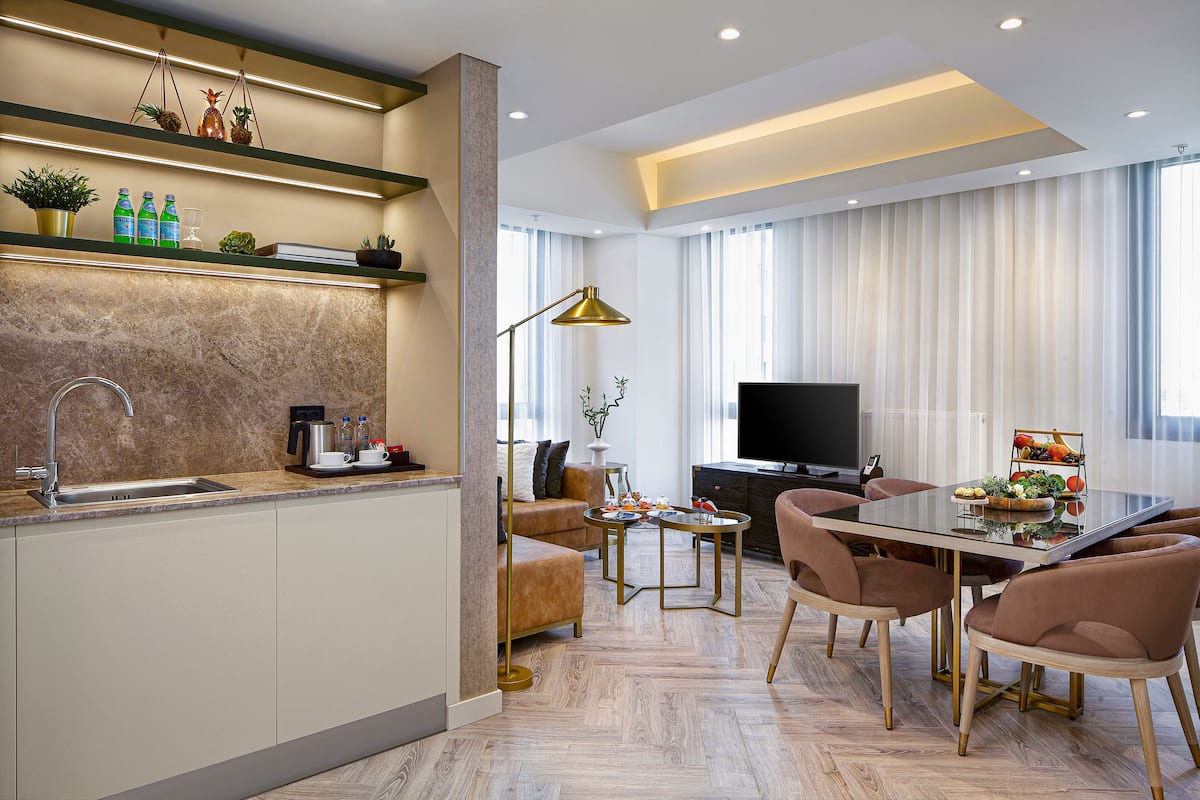 A modern kitchen with a built-in island, a dining area with a glass table, and a living room with a flat-screen TV.