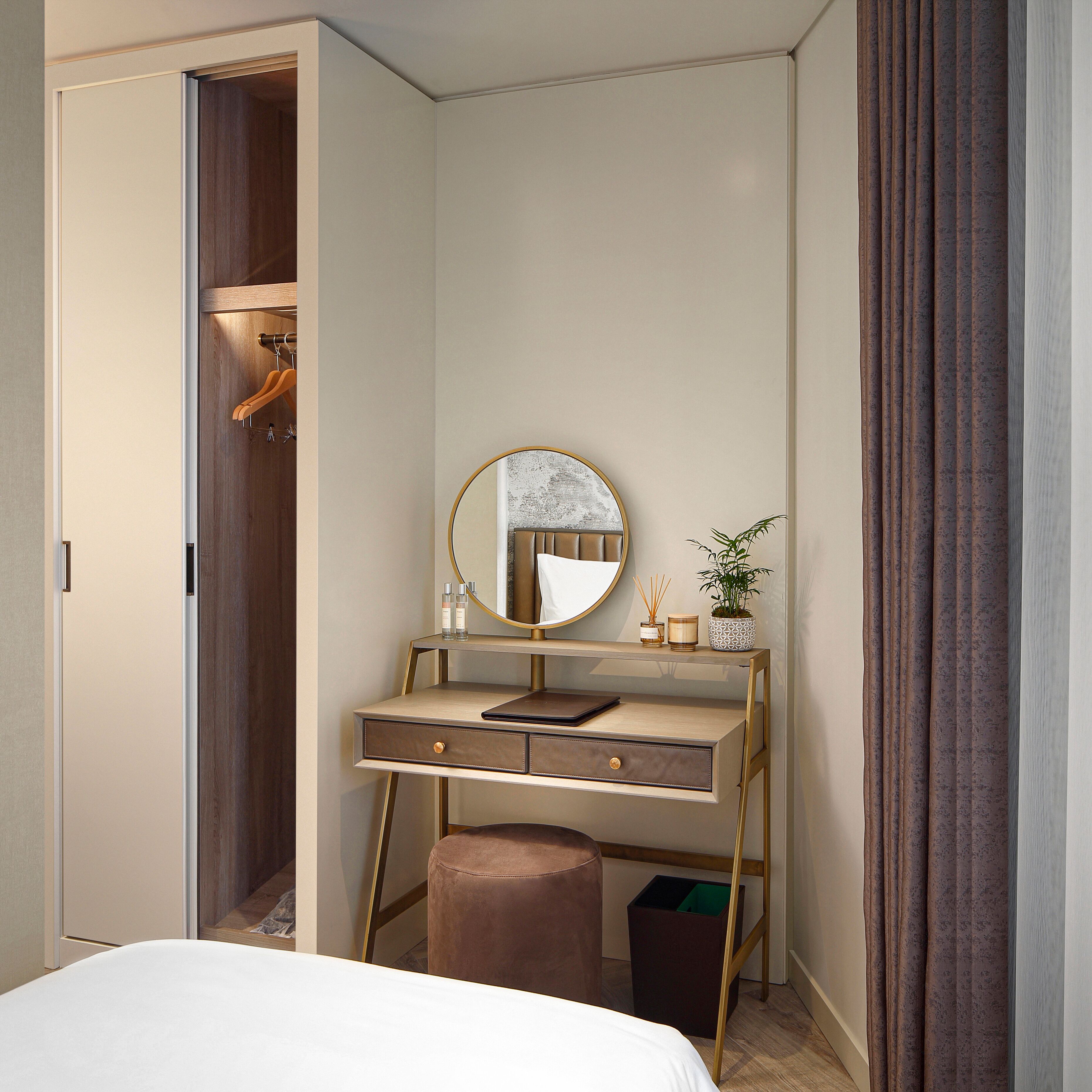 A bedroom with a bed, a vanity with a mirror, a small stool, and a wardrobe.
