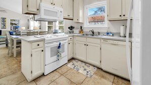 A modern kitchen with white cabinetry, a built-in microwave, and a large window. - West Destin!  3 blks to beach! Front & back porch! Walk to shopping/restaurants (Destin)