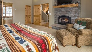 A bedroom with a large bed, a fireplace, a television mounted on the wall, and a staircase leading to another level. - Ski-in/Ski-out w/private hot tub and stunning views in Cowboy Heaven - The Moose Lodge (Big Sky)