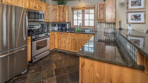 A kitchen with wooden cabinets, stainless steel appliances, a granite countertop, and a window with a view. - Ski-in/Ski-out w/private hot tub and stunning views in Cowboy Heaven - The Moose Lodge (Big Sky)