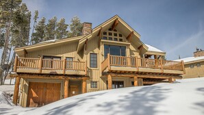 A two-story log cabin with a balcony, large windows, and a snow-covered roof. - Ski-in/Ski-out w/private hot tub and stunning views in Cowboy Heaven - The Moose Lodge (Big Sky)