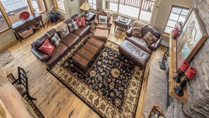 A spacious living room with a large sectional sofa, a wooden coffee table, and a patterned rug. - Ski-in/Ski-out w/private hot tub and stunning views in Cowboy Heaven - The Moose Lodge (Big Sky)